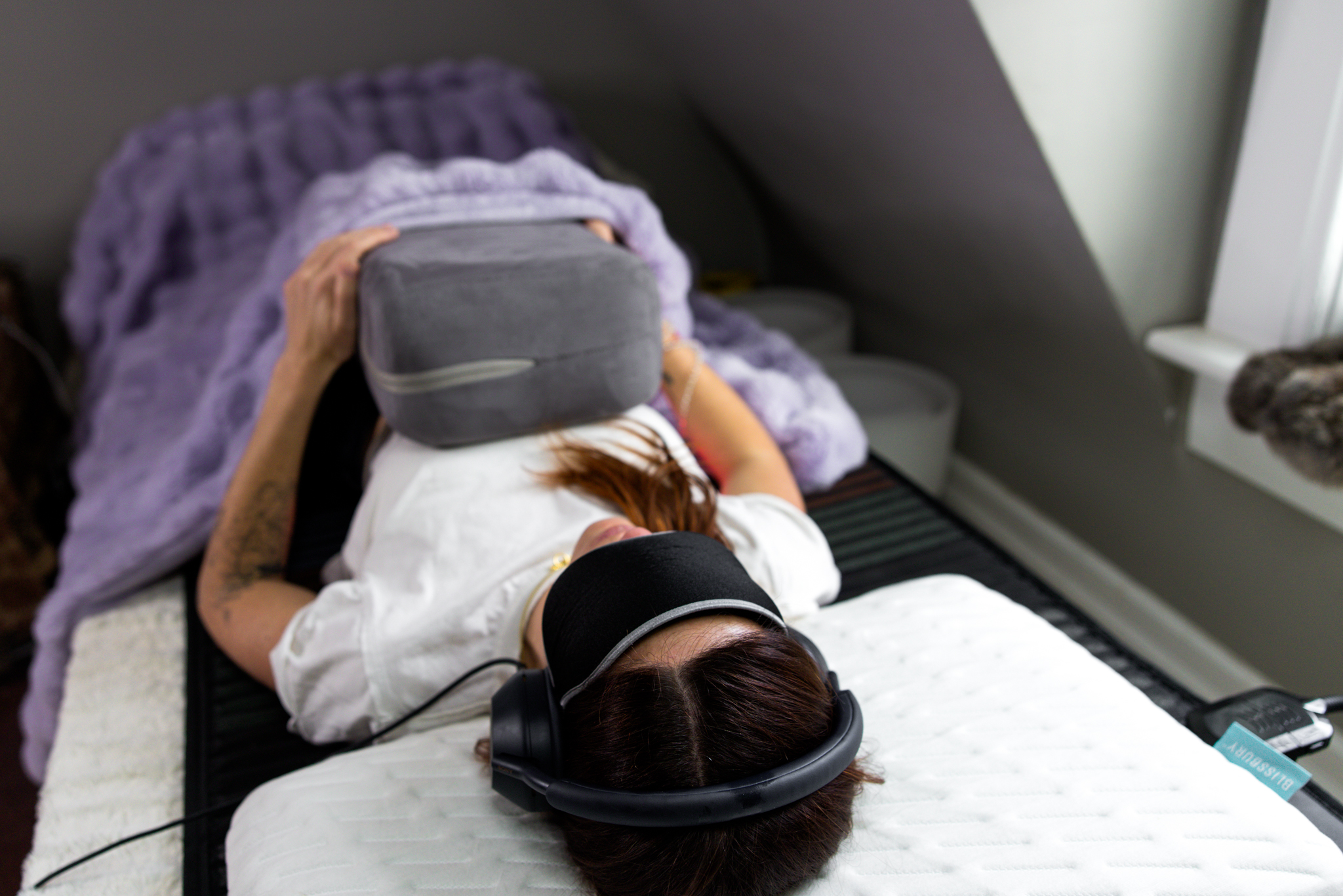VAVE™ Frequency Therapy Session on VAVE™ Platform – Resonant Wellnest Woman relaxing on a VAVE™ platform during a frequency therapy session with headphones and eye mask
